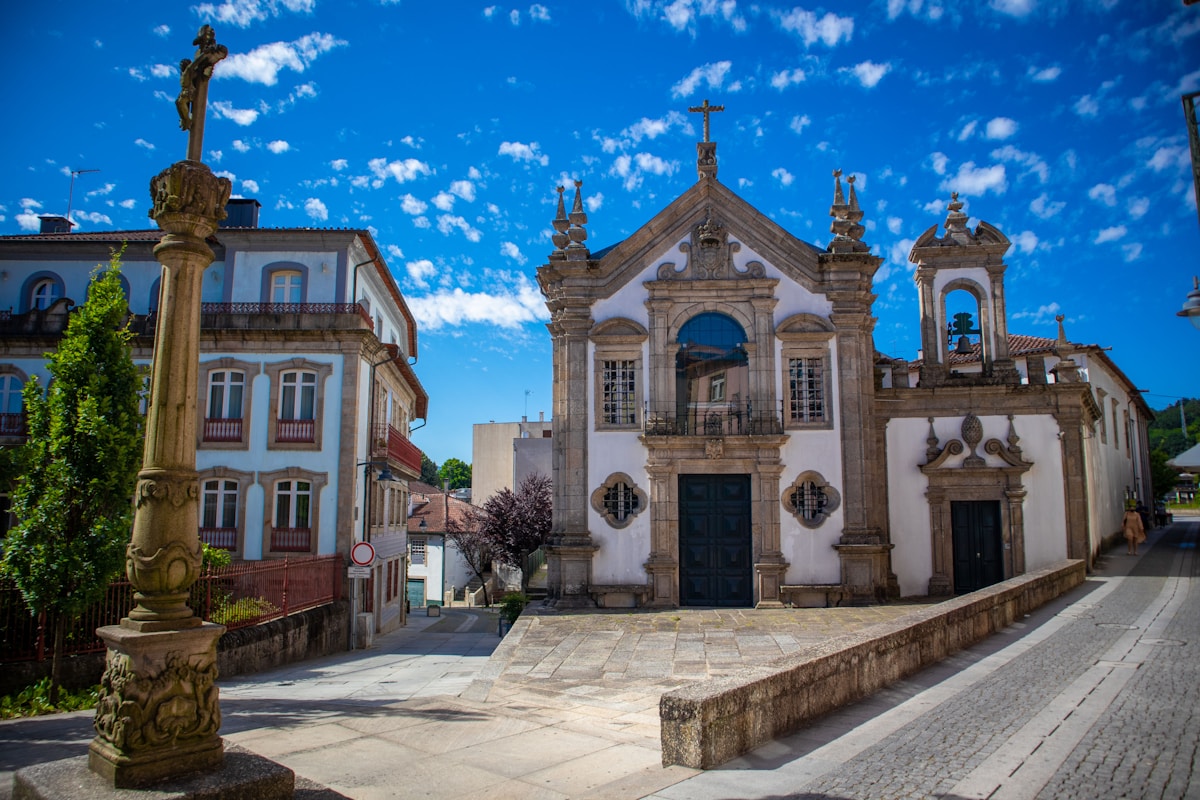 Baroque Portuguese church with ornate facade and stone cross on a cobblestone square
