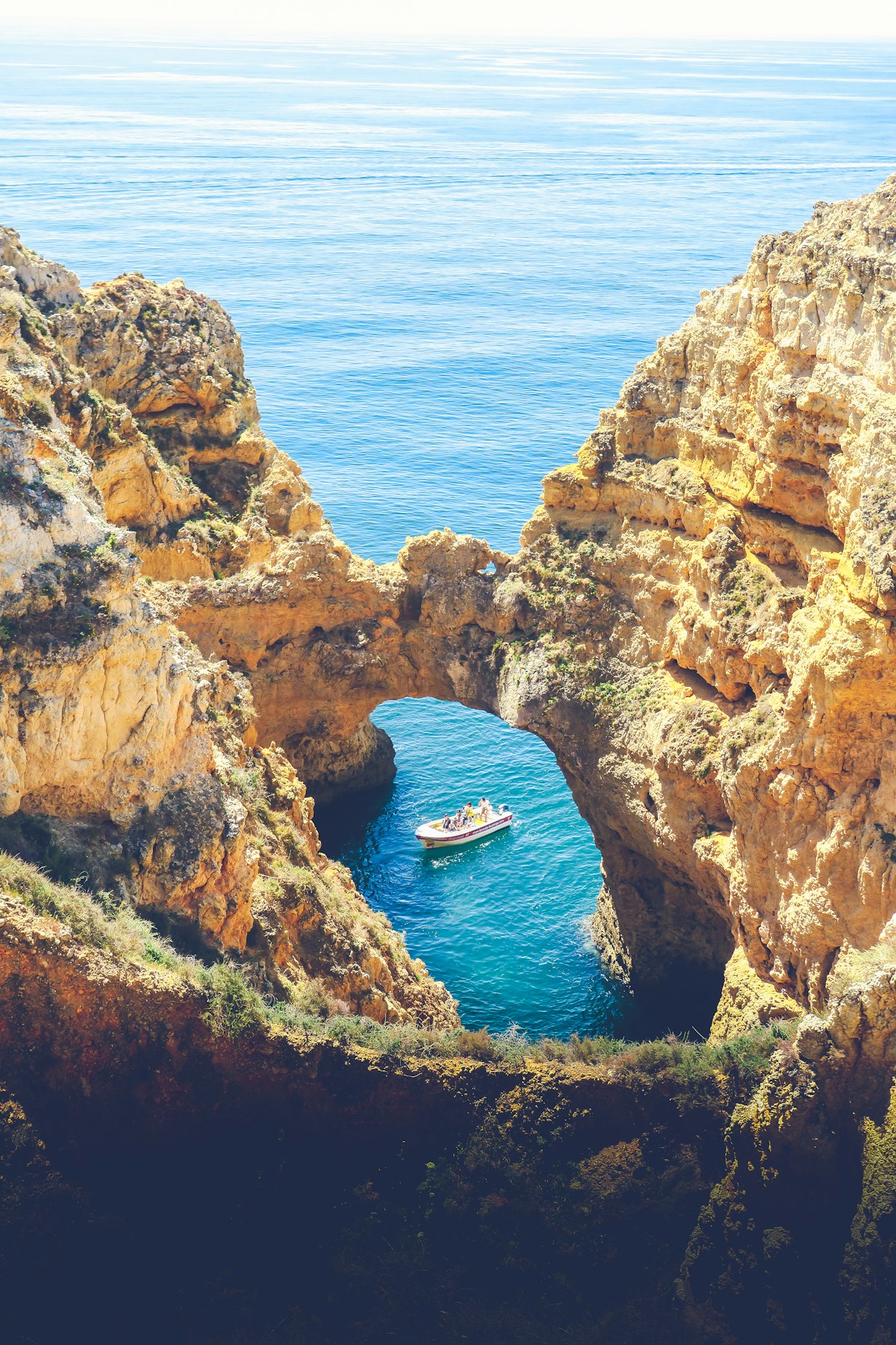 Blue and white boat sailing through golden limestone rock arches at Ponta da Piedade, Lagos, Algarve, Portugal