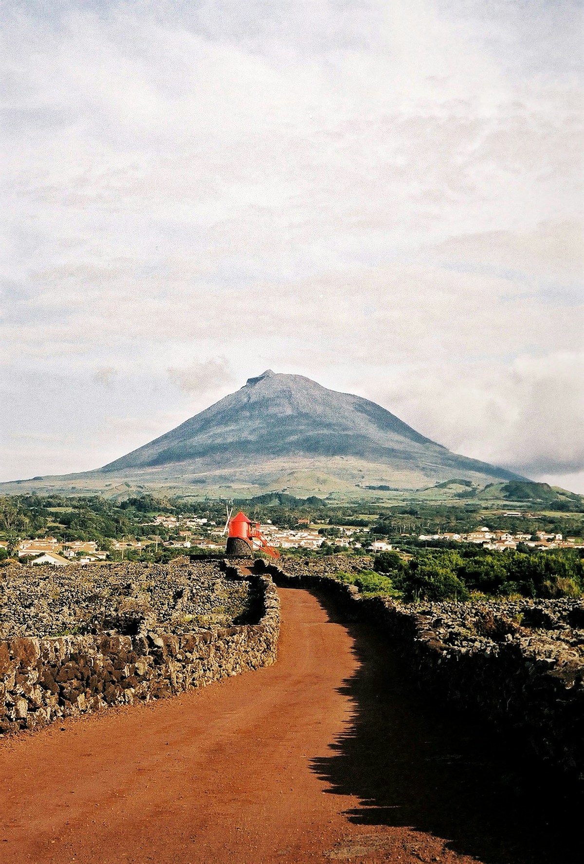 Red windmill on a dirt road leading through lava fields towards Pico mountain's volcanic cone, Pico island, Azores, Portugal
