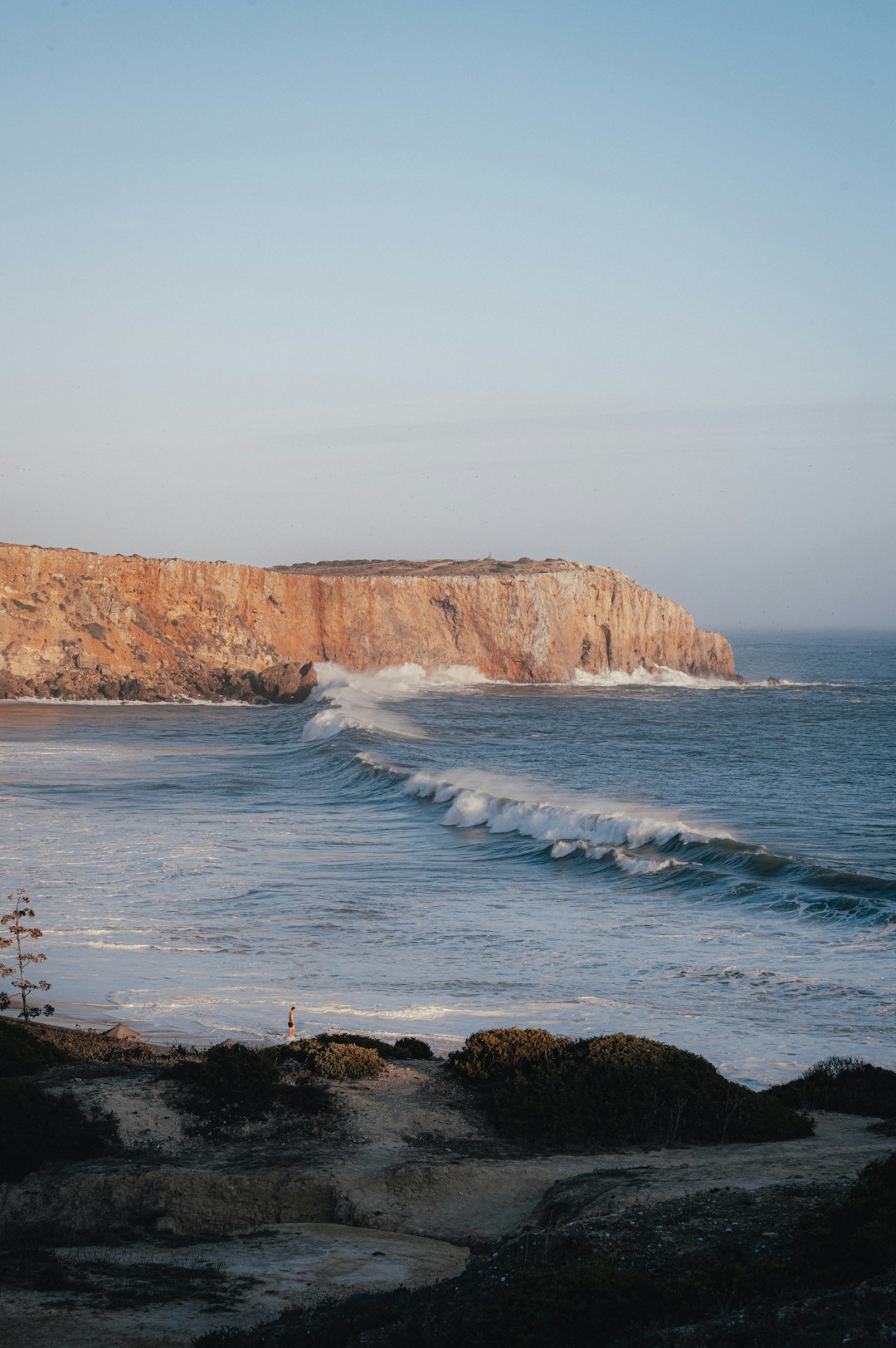 Waves breaking on a Sagres beach with the characteristic red cliffs of the Algarve in the background at sunset