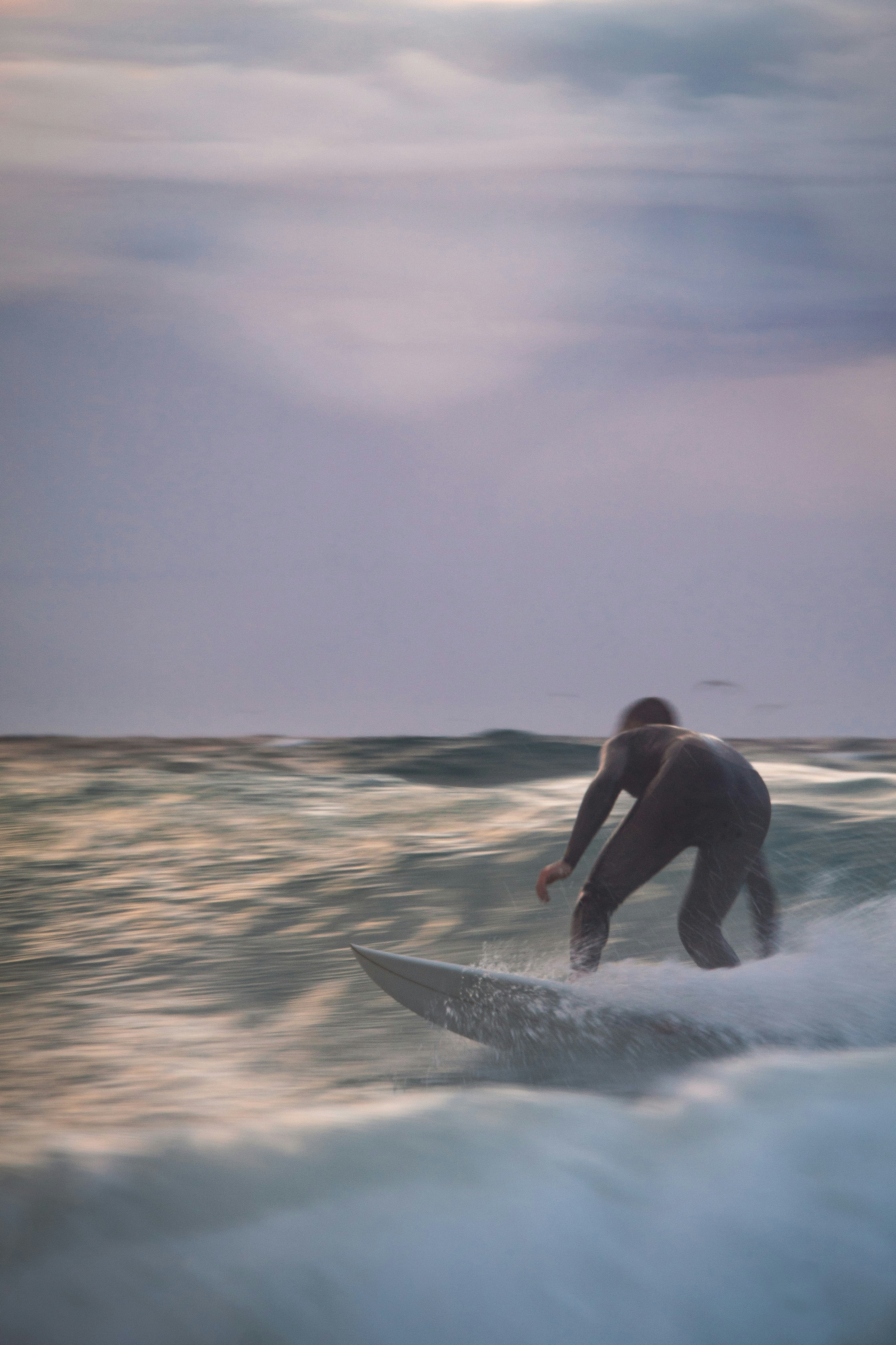 Surfer riding a wave at dusk on Portugal's Atlantic coast in a full wetsuit