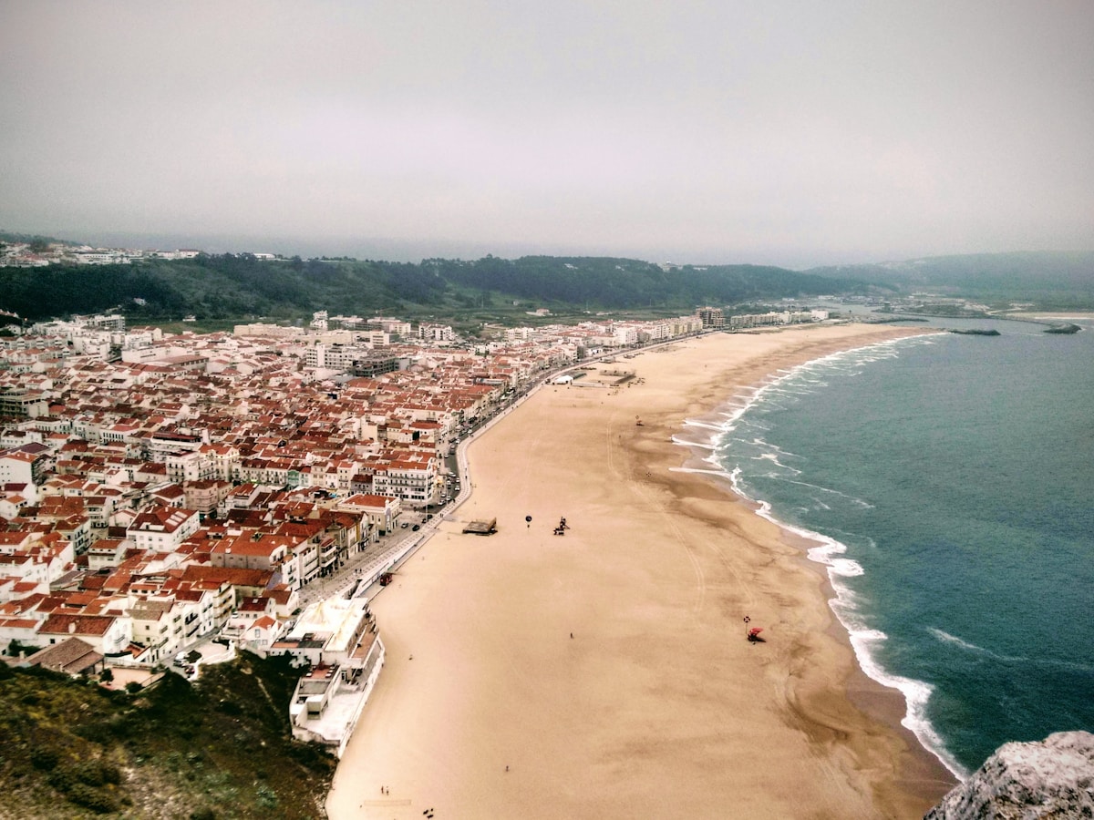 Aerial view of Nazare, Portugal, showing the town rooftops, long sandy beach, and Atlantic Ocean