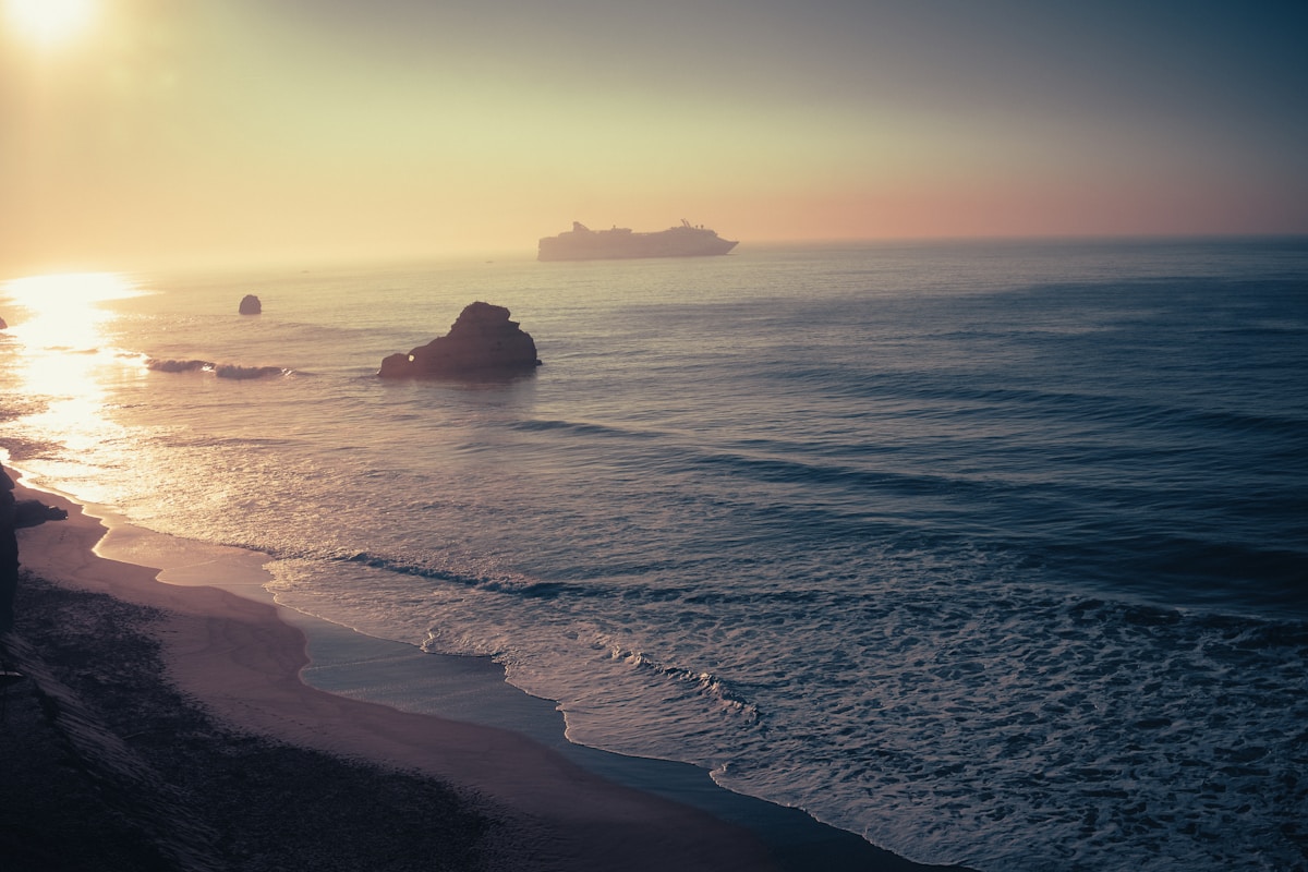 Sandy beach at sunset with rock formation and cruise ship offshore, Portimão, Algarve, Portugal