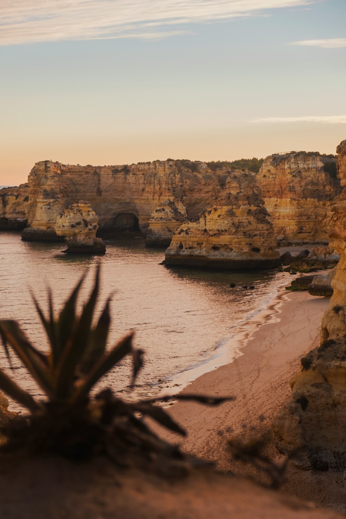 Golden limestone cliff arch and sea cave above turquoise water at sunset, Algarve, Portugal