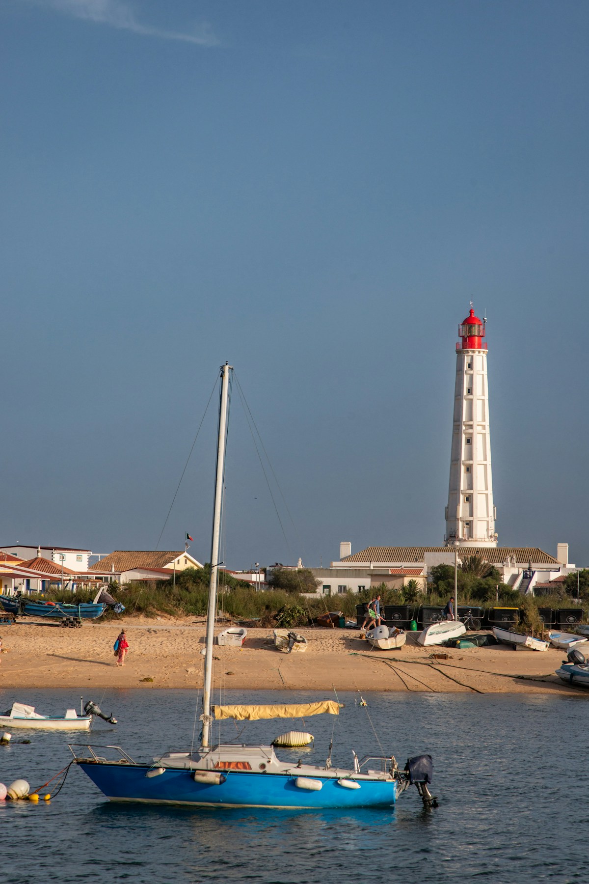 Blue sailboat moored in the Ria Formosa lagoon with the Ilha do Farol lighthouse, Faro, Portugal