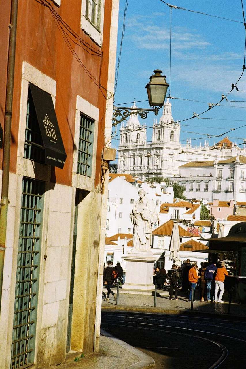 Rua do bairro da Alfama com mosteiro branco e estátua histórica, Lisboa, Portugal