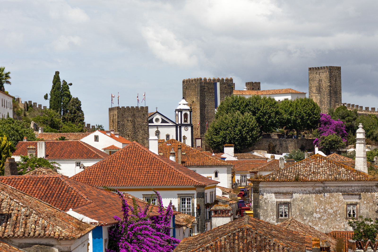 Óbidos rooftops and medieval castle walls with purple bougainvillea in bloom, Silver Coast, Portugal