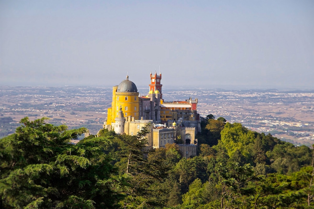 Pena Palace with its yellow and red towers rising above the forested hills of Sintra, Portugal