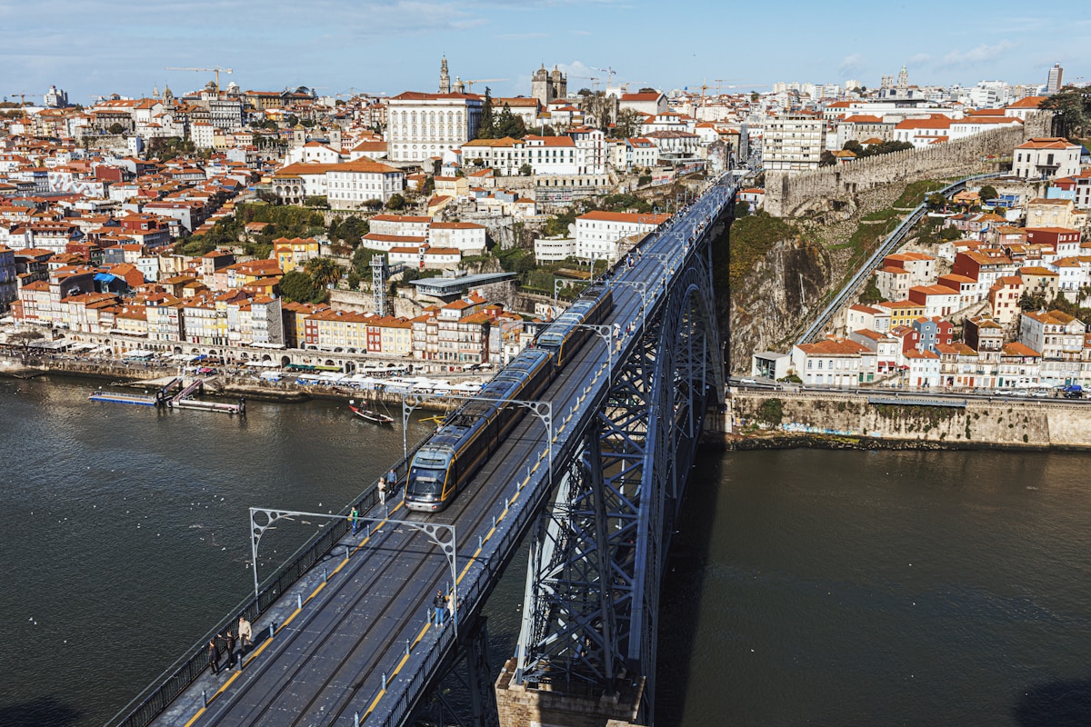 Train crossing Ponte Dom Luís I over the Douro River in Porto, with the city's terracotta rooftops and cathedral rising behind