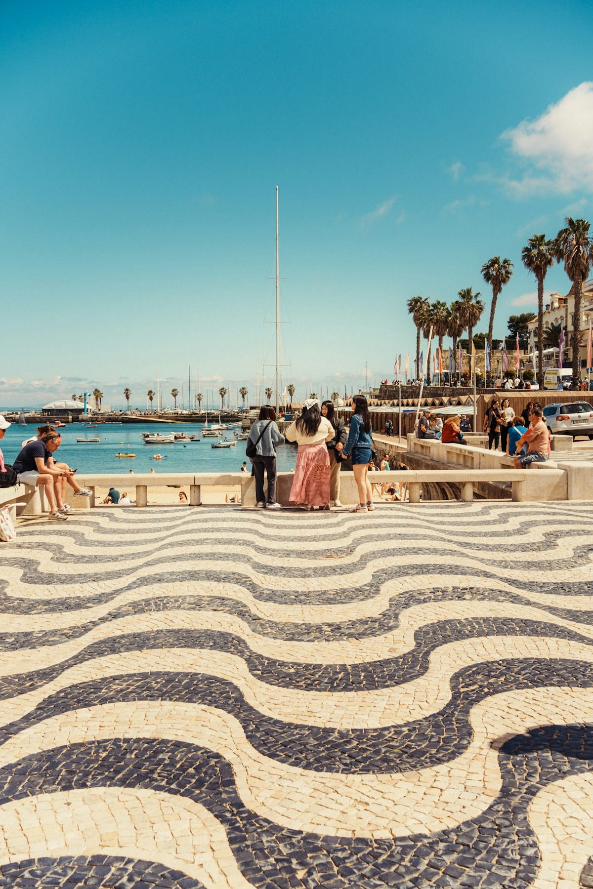 Cascais waterfront promenade with its distinctive black and white wave-patterned paving, palm trees and marina in the background, Portugal