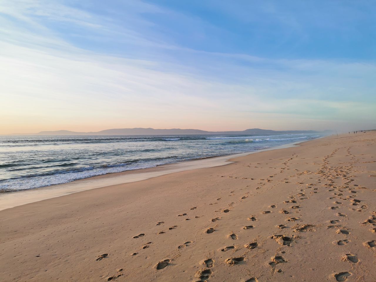 Badegäste unter Strohschirmen an den breiten weißen Stränden von Comporta mit dem blauen Atlantik dahinter