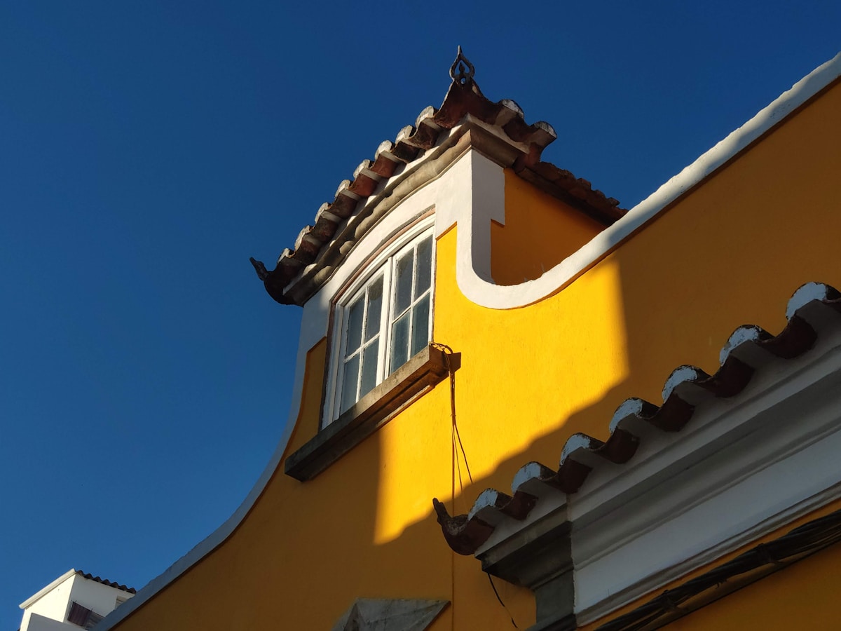 Yellow building with white trim and traditional terracotta roof tiles under a deep blue sky in Faro old town, Algarve, Portugal