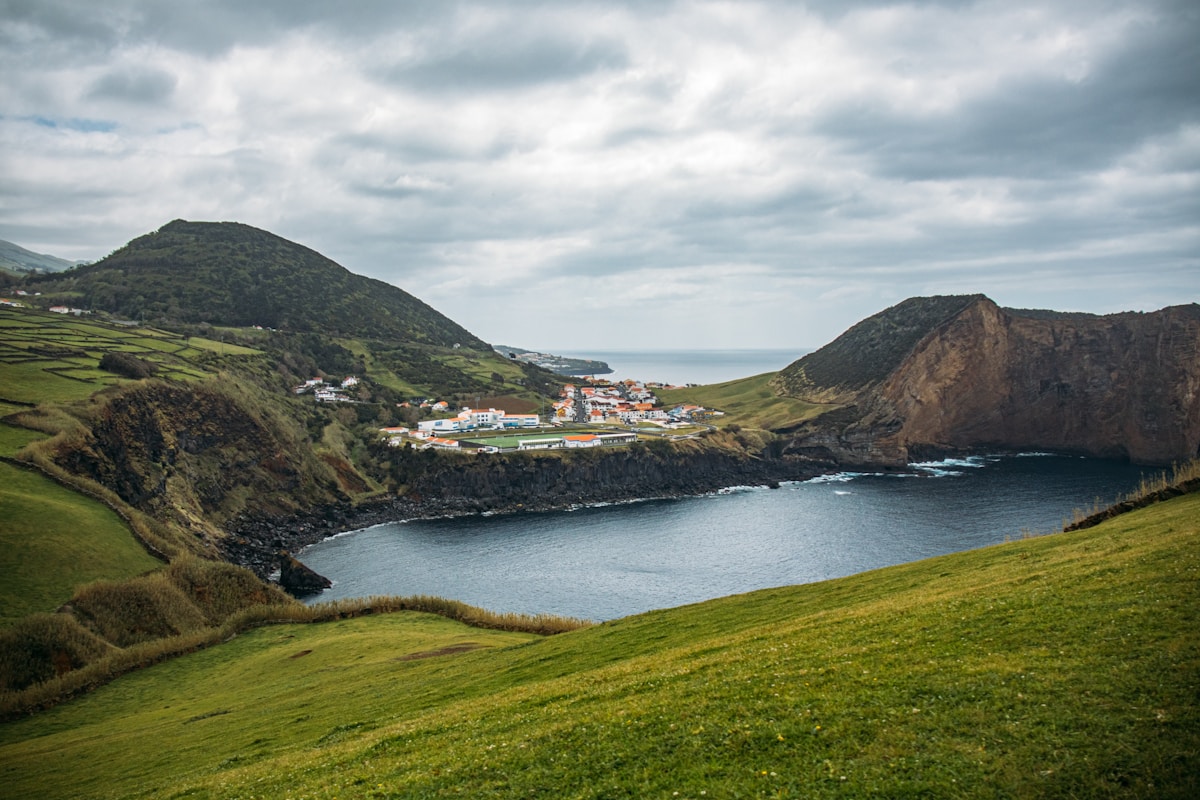 Small coastal village nestled in a bay surrounded by dramatic green volcanic hills, São Jorge island, Azores, Portugal