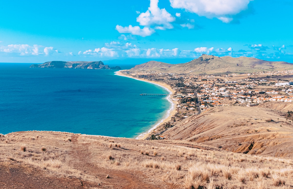 Panoramic aerial view of Porto Santo island showing the sweeping 9km golden beach, the town of Vila Baleira, and arid volcanic hills against a blue Atlantic