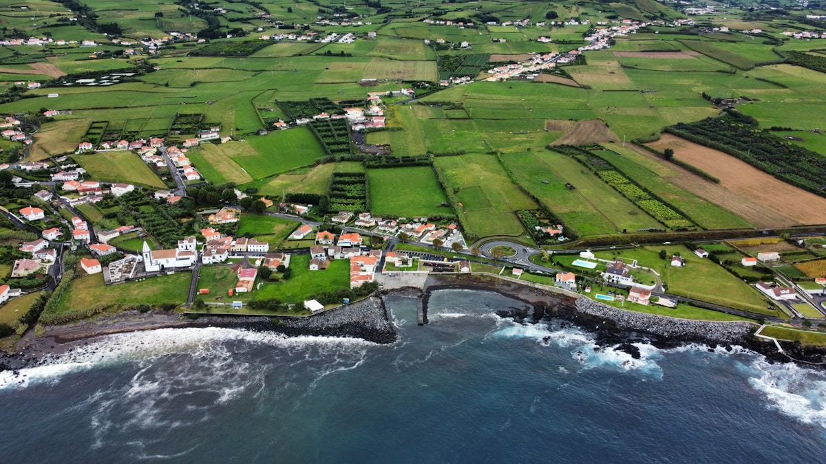 Aerial view of a Faial coastal village with volcanic fields and patchwork green fields, Azores, Portugal