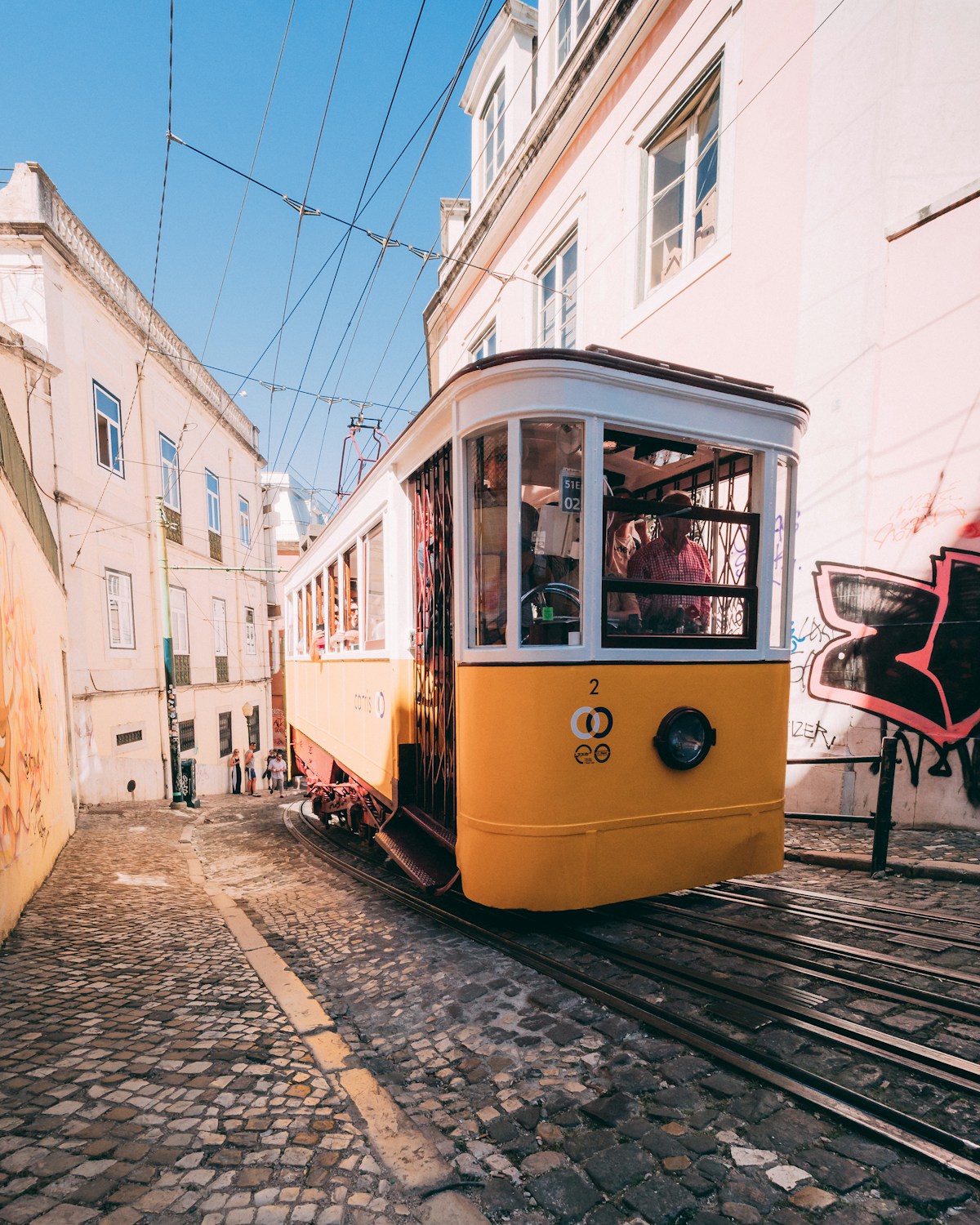 Yellow and white tram climbing a steep cobblestone hill in Lisbon - getting around Portugal by public transport