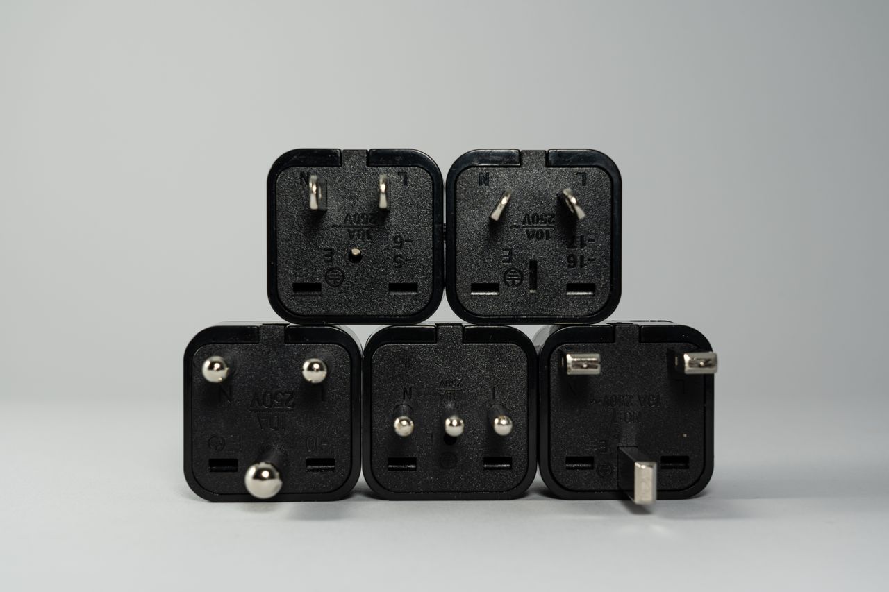 Cinco adaptadores de viagem pretos com fichas diferentes sobre fundo cinzento