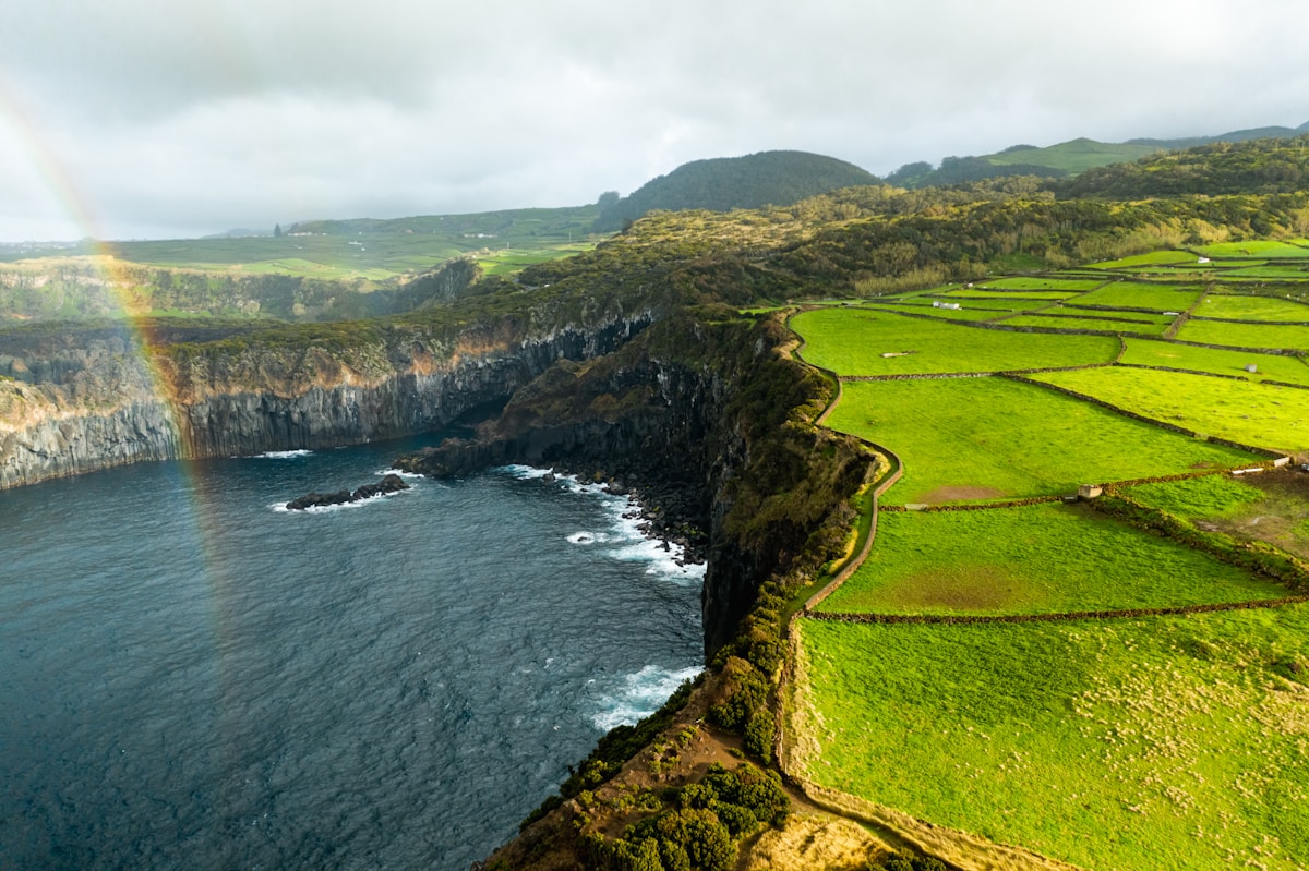 Aerial view of dramatic Azores coastal cliffs with green fields and a rainbow, Portugal