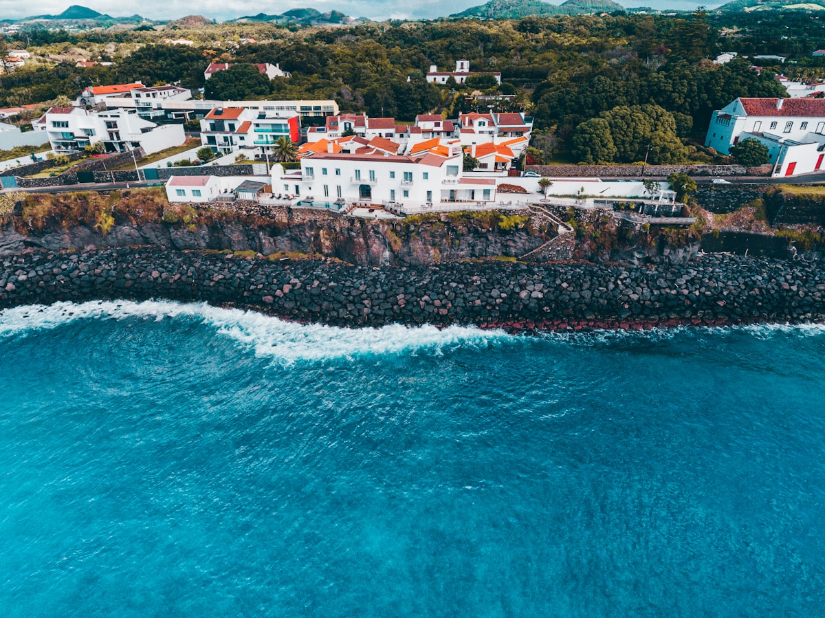 Aerial view of houses on basalt sea cliffs with turquoise Atlantic waves, Ponta Delgada, Azores, Portugal