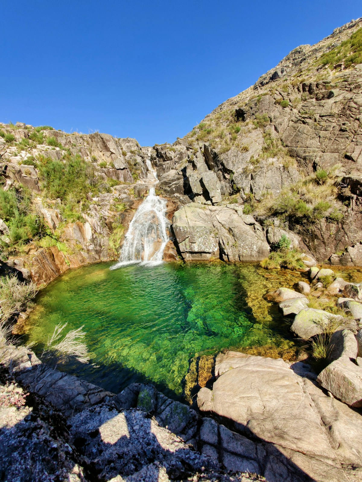 Emerald waterfall pool with a cascade falling over rocky granite cliffs in Serra de Gerês, Peneda-Gerês National Park, Portugal