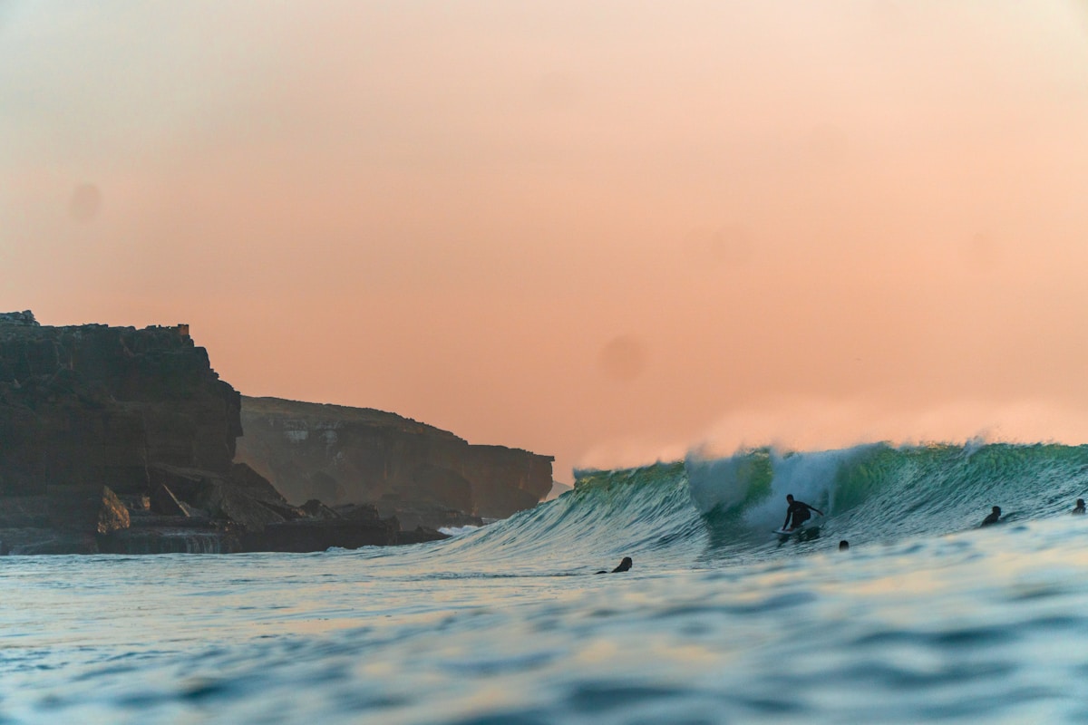 Surfers riding waves at sunset beneath the cliffs of Ericeira, Portugal