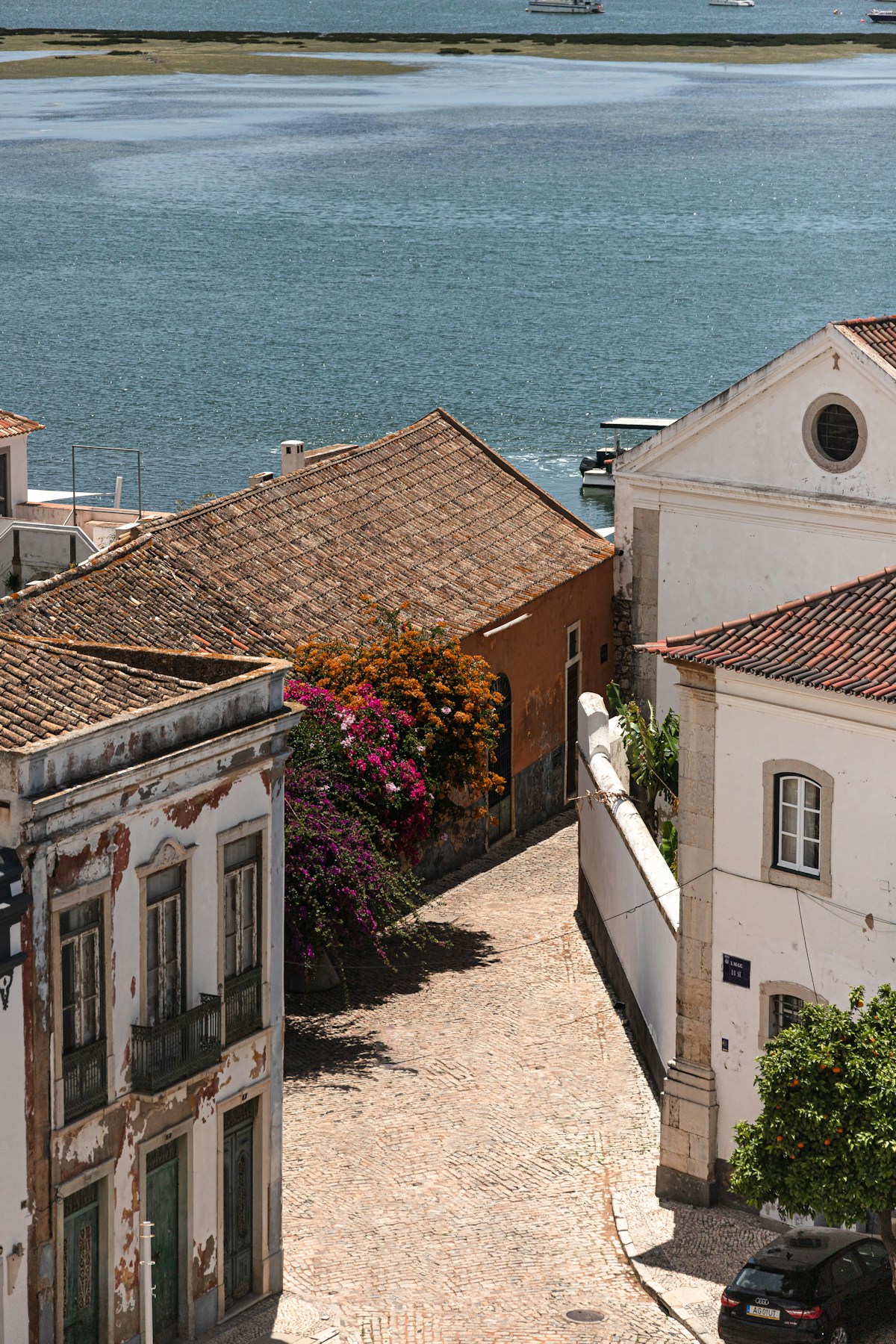 Cobblestone street in Faro old town with flowering bougainvillea and the Ria Formosa lagoon behind
