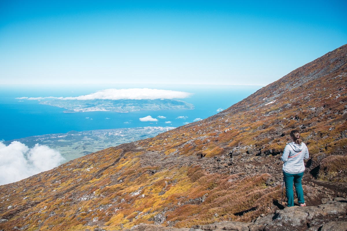 Hiker on the volcanic slopes of Pico mountain overlooking the Atlantic Ocean and Faial island, Azores, Portugal