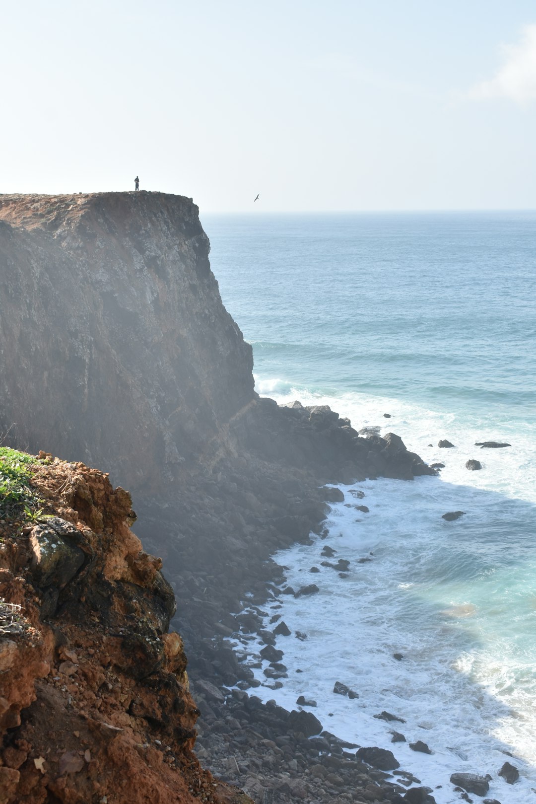 Dramatic cliffs at Sagres with waves crashing against the Atlantic coast and a figure standing at the edge