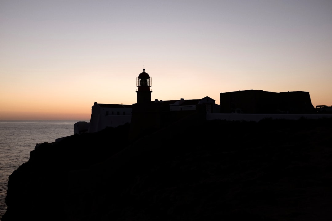 Silhouette of the Cape St. Vincent lighthouse and fortress buildings against a sunset sky at Sagres