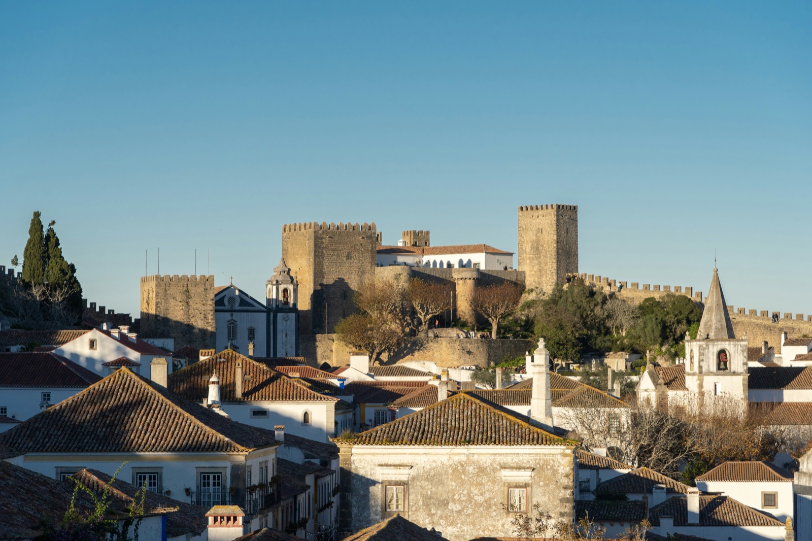 Medieval castle and battlements of Óbidos rising above terracotta-roofed whitewashed buildings, Silver Coast, Portugal